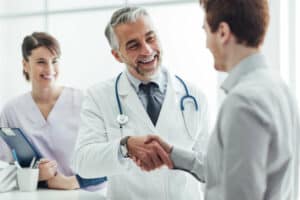 A male doctor and his male patient smiling and shaking hands