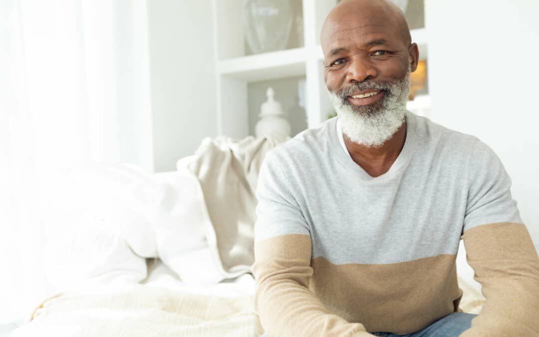 Middle aged African American male sitting on his bed and smiling at the camera