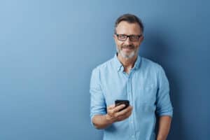 Middle aged man holding a phone and smiling at the camera